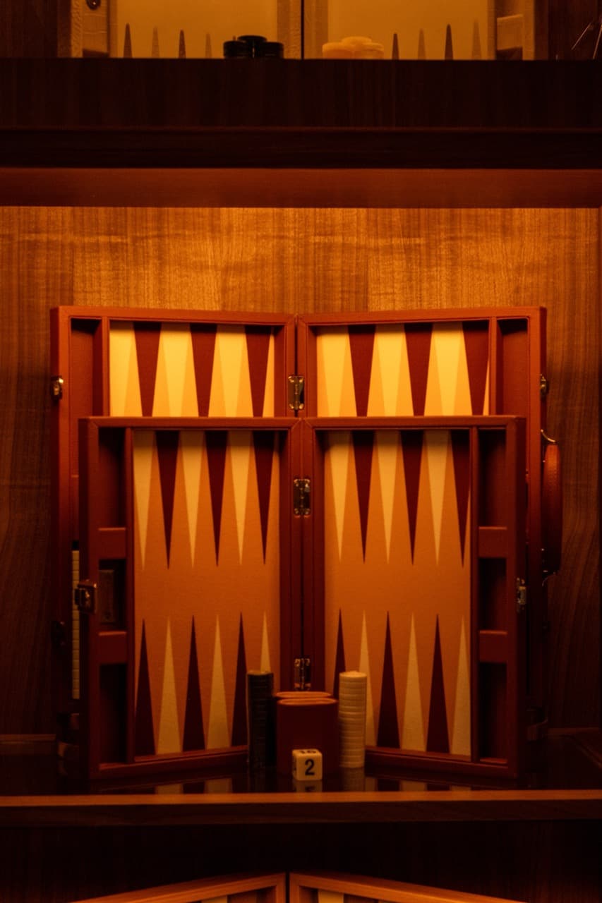 An open leather backgammon board lit warm against a walnut wall at 7 Spring.